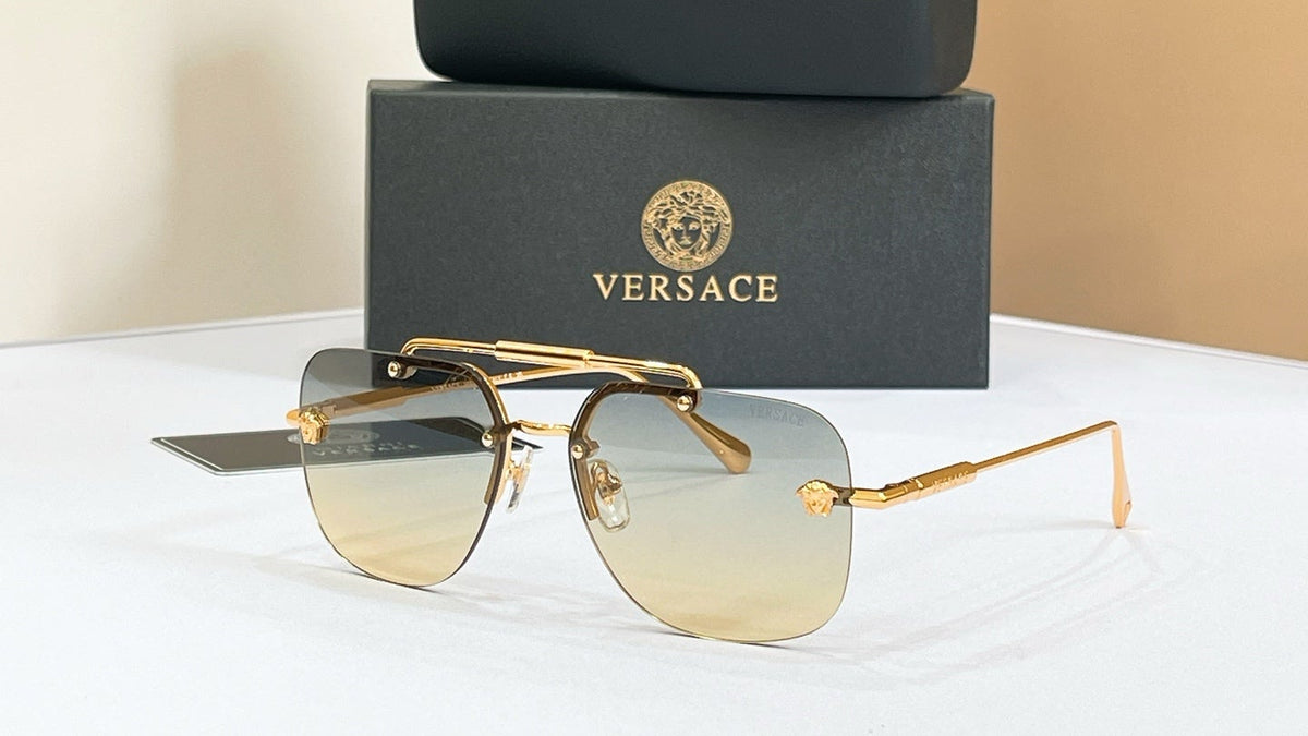 Versace sunglasses with gold frame and gradient lenses, placed on a white surface with a beige and brown background.